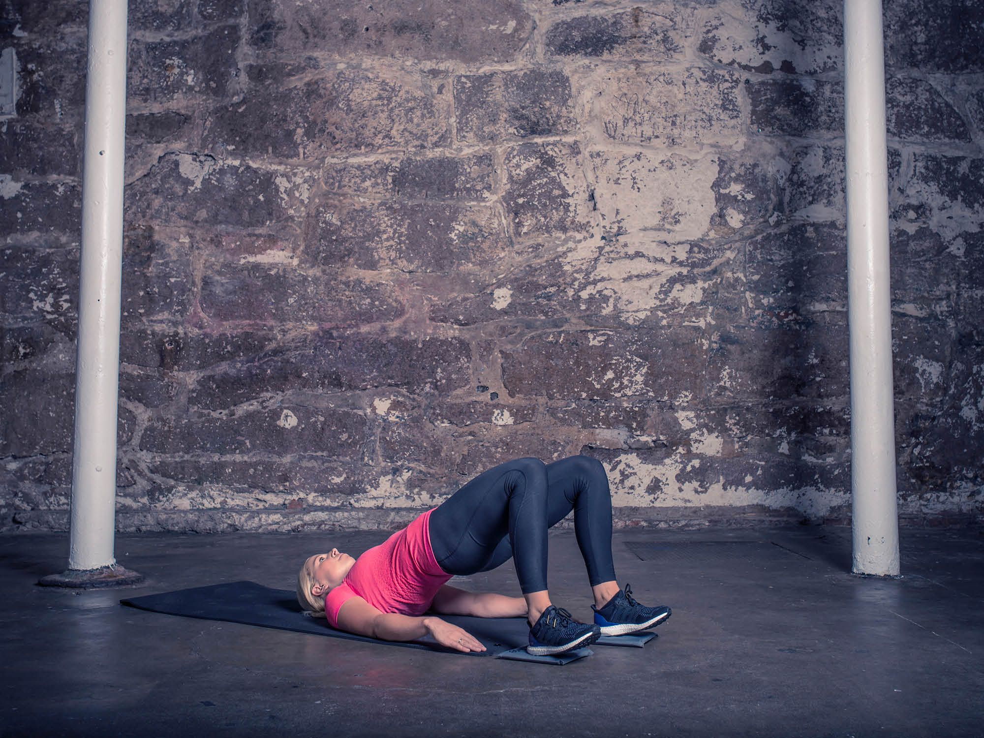 En kvinne ligger på en sklimatte i en treningshall, med bena bøyd og armene langs siden.