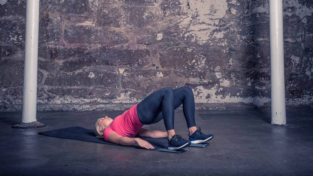 En kvinne ligger på en sklimatte i en treningshall, med bena bøyd og armene langs siden.