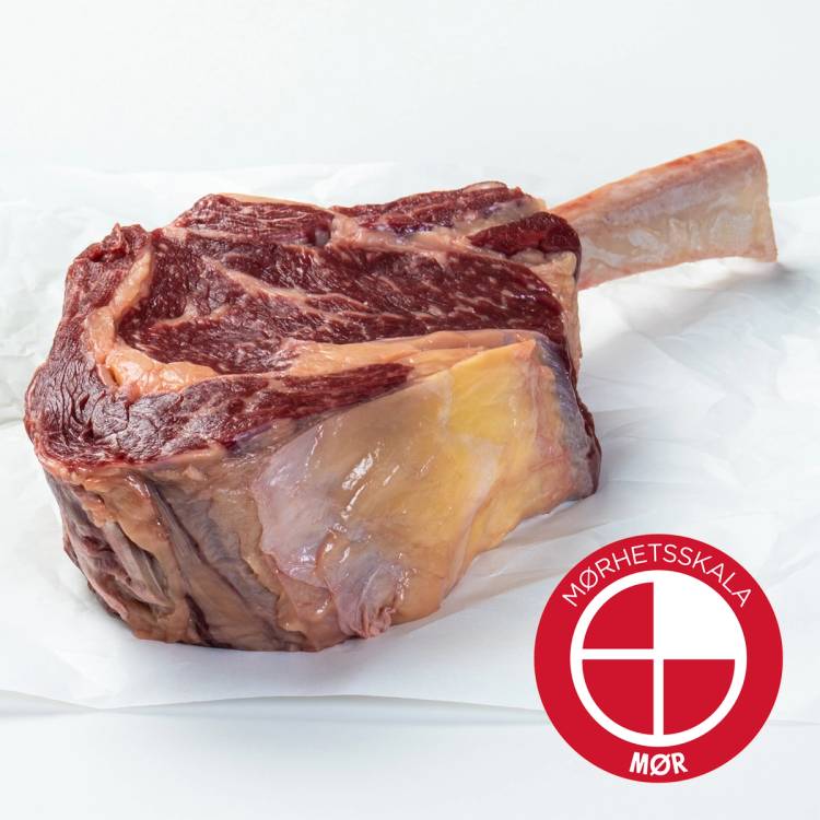 Et stykke Angus Tomahawk-biff med bein, lagt på hvitt papir, med Mørhetsskala-logo i hjørnet.