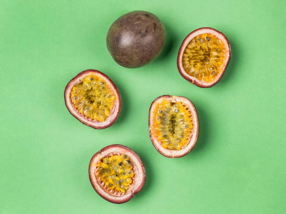 En hel pasjonsfrukt og fire halverte pasjonsfrukter med gul fruktkjøtt og svarte frø på en grønn bakgrunn.