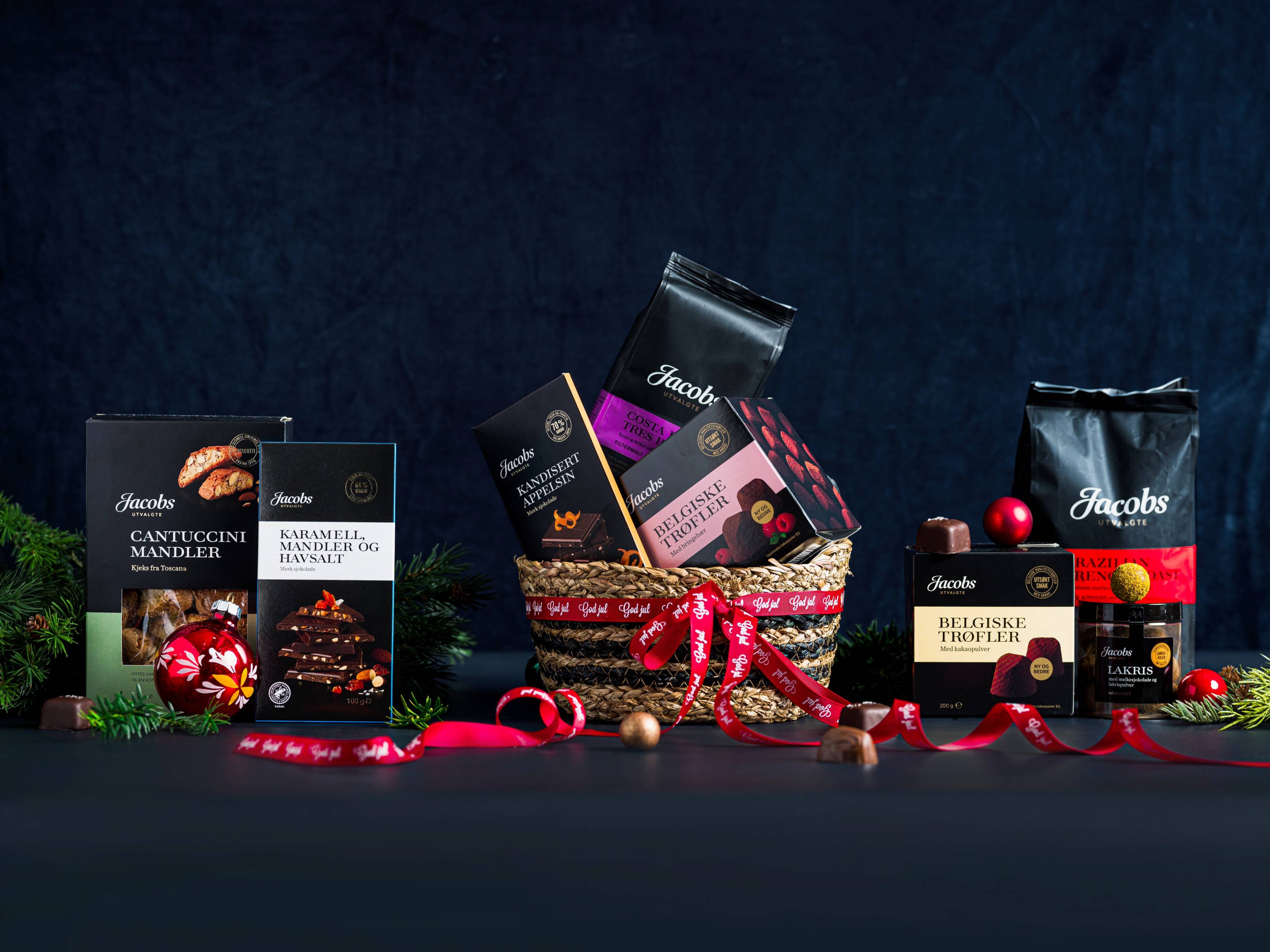 Ulike julegaver med sjokolade og konfekt, dekorert med granbar og røde bånd, på en mørk bakgrunn.