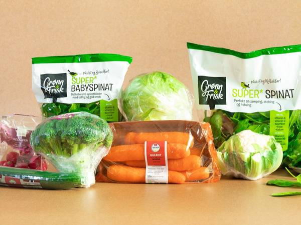 Ferske grønnsaker som gulrøtter, hodekål og spinat på et kjøkkenbord, med emballasje av babyspinat og superspinatsalat i bakgrunnen.