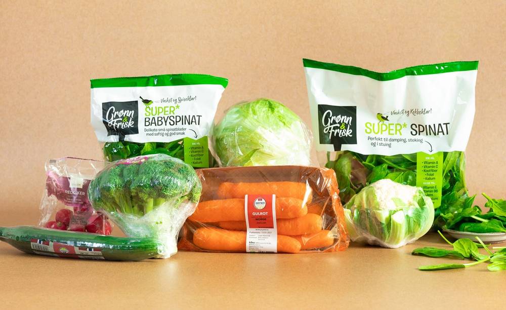 Ferske grønnsaker som gulrøtter, hodekål og spinat på et kjøkkenbord, med emballasje av babyspinat og superspinatsalat i bakgrunnen.