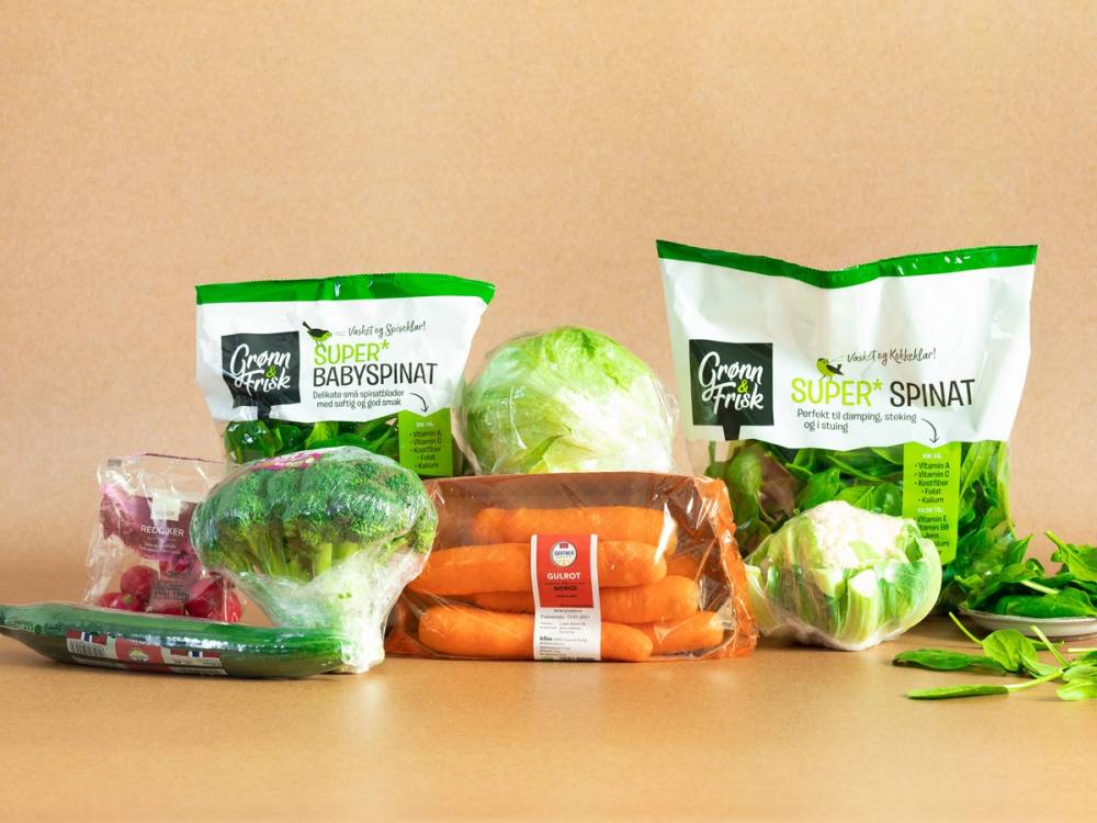 Ferske grønnsaker som gulrøtter, hodekål og spinat på et kjøkkenbord, med emballasje av babyspinat og superspinatsalat i bakgrunnen.