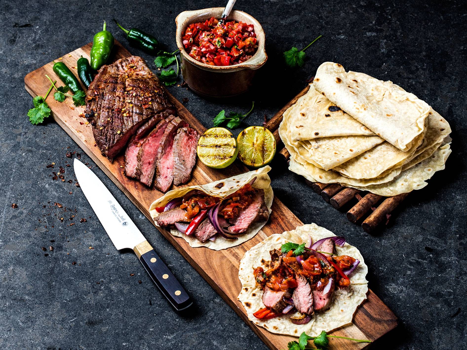 Flank-steak fajitas med tortillas, pico de gallo og lime på et skjærebrett.