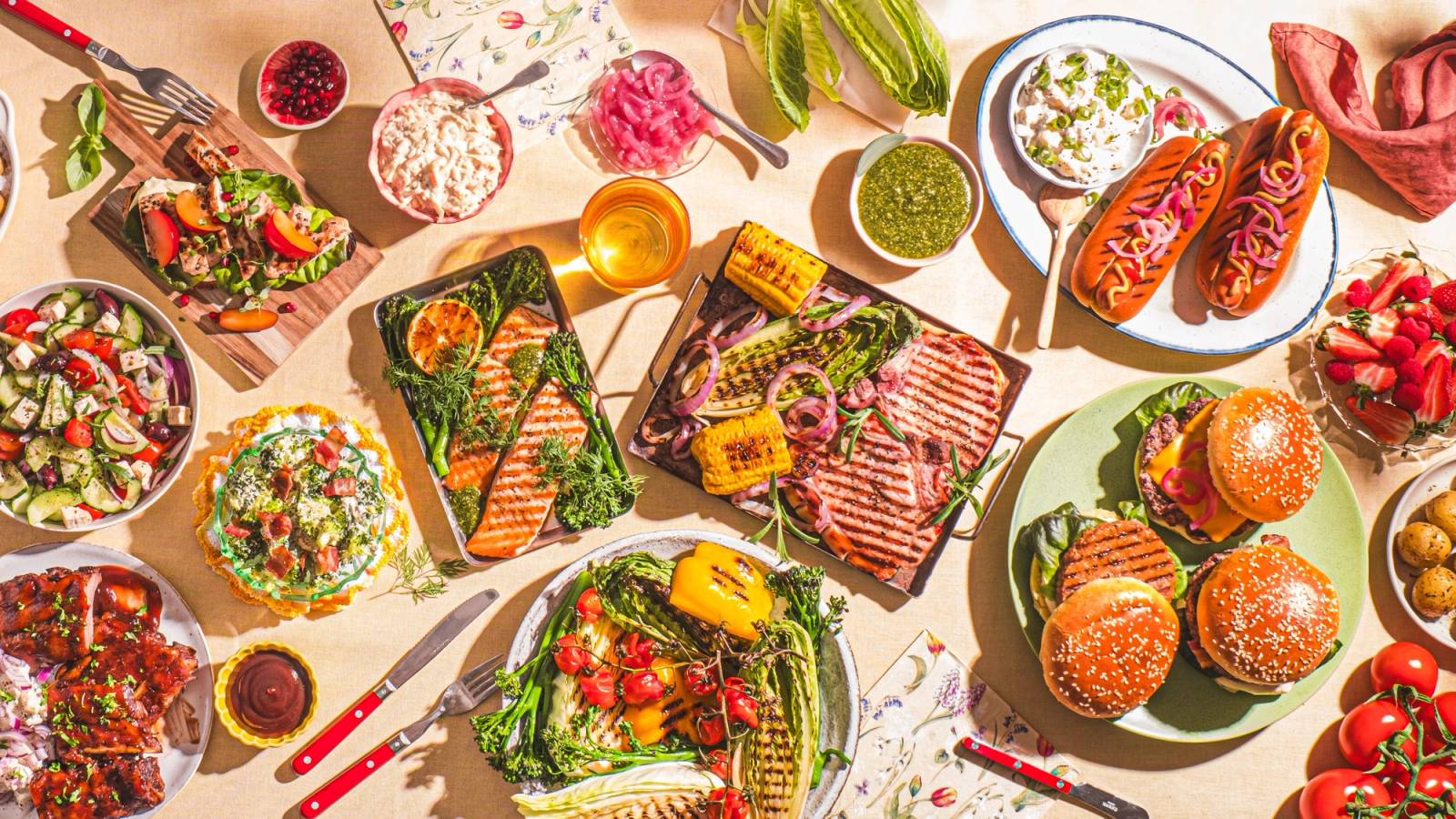 Et bord dekket med ulike sommerretter, salater, brød og frukt, med sollys som skinner over maten.