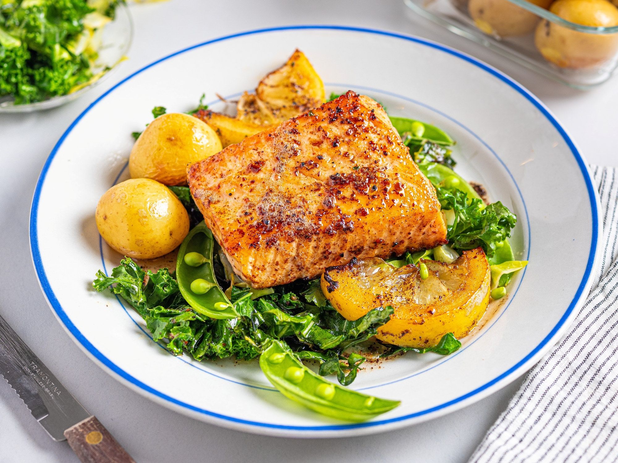 Laksefilet med stekt kål og små poteter på en hvit tallerken med blå kant.