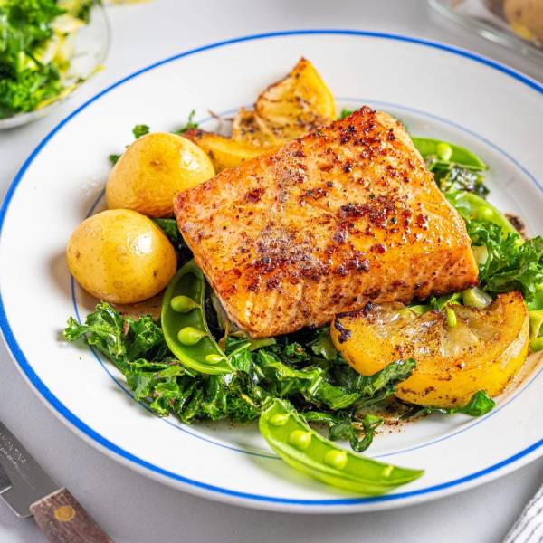 Laksefilet med stekt kål og små poteter på en hvit tallerken med blå kant.