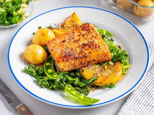 Laksefilet med stekt kål og små poteter på en hvit tallerken med blå kant.