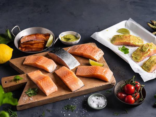 Fiskekjøtt og laksefileter på et skjærebrett, med sitron, tomater og krydder rundt om, klar for sommerkampanje.