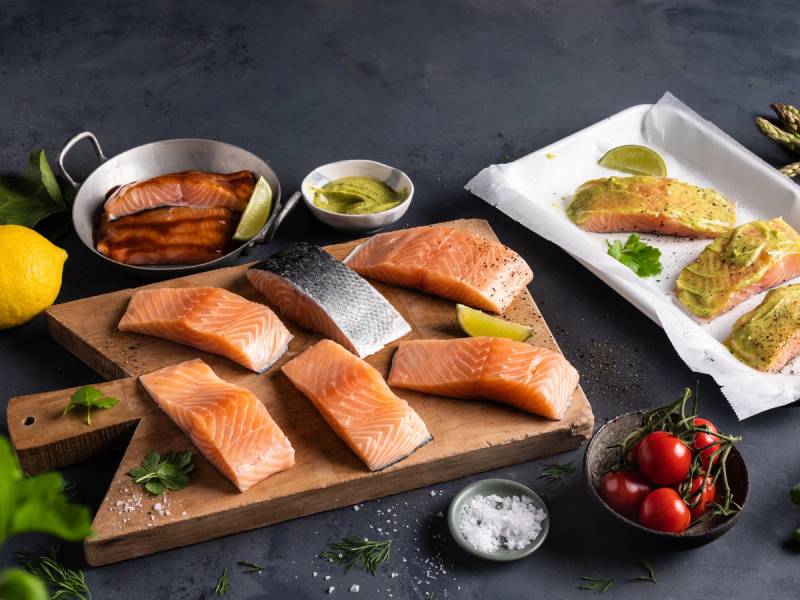 Fiskekjøtt og laksefileter på et skjærebrett, med sitron, tomater og krydder rundt om, klar for sommerkampanje.