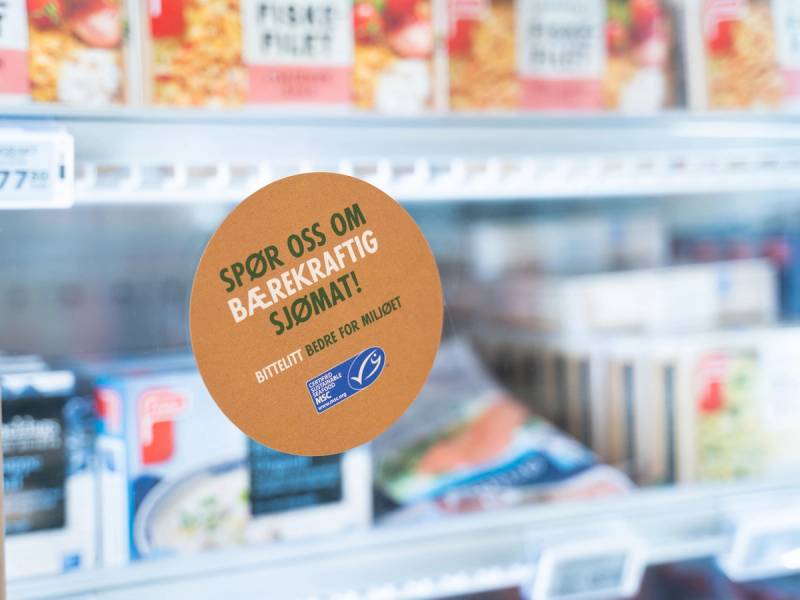 En butikkhylle med meieriprodukter og en rund, oransje plakat som oppfordrer til å spore oss om bærekraftig sjømat.