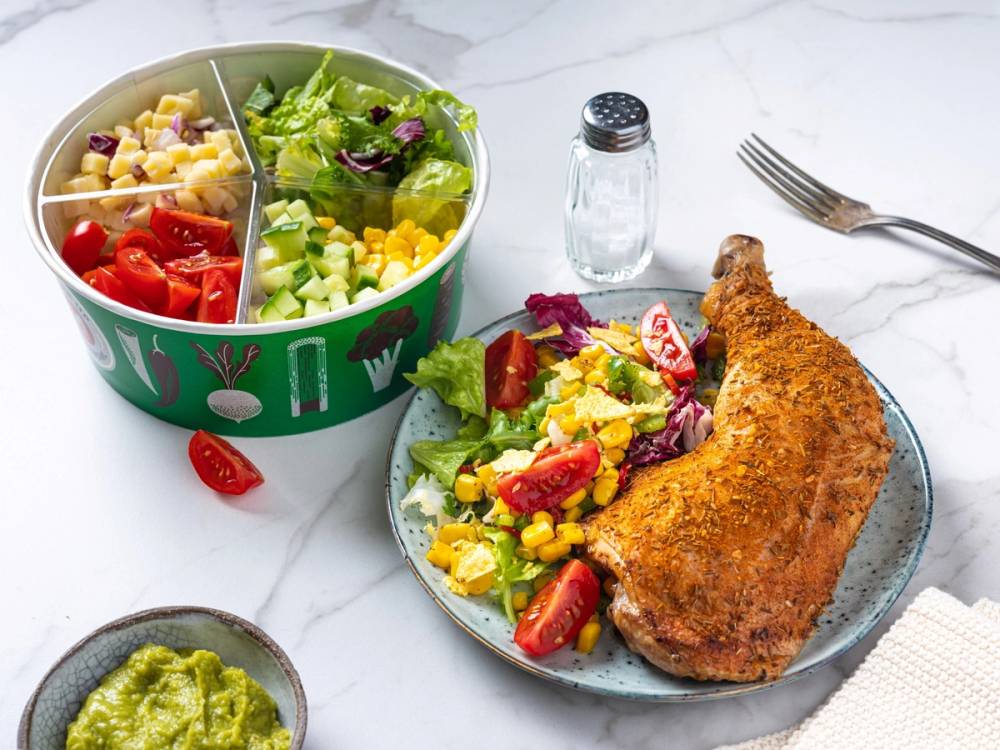 En salatbar med kyllinglår og en tallerken med salat og kyllinglår ved siden av, samt en liten skål med guacamole og en salt- og pepperbøtte på bordet.