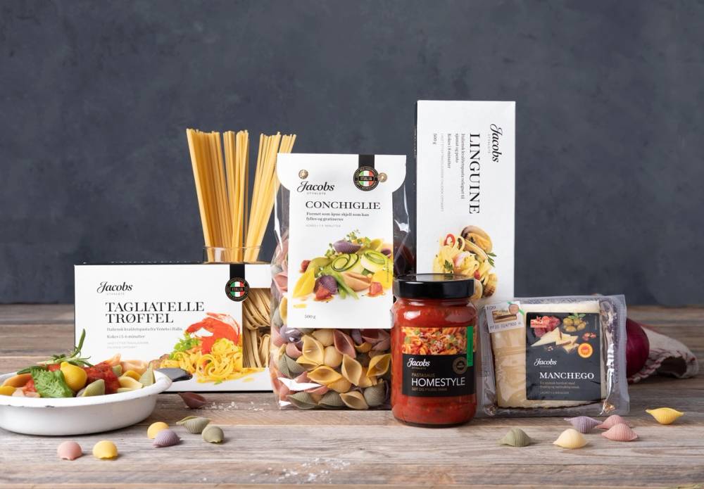 Ulike typer pasta, en pastasaus og manchego-ost på et kjøkkenbord med en mørk bakgrunn.