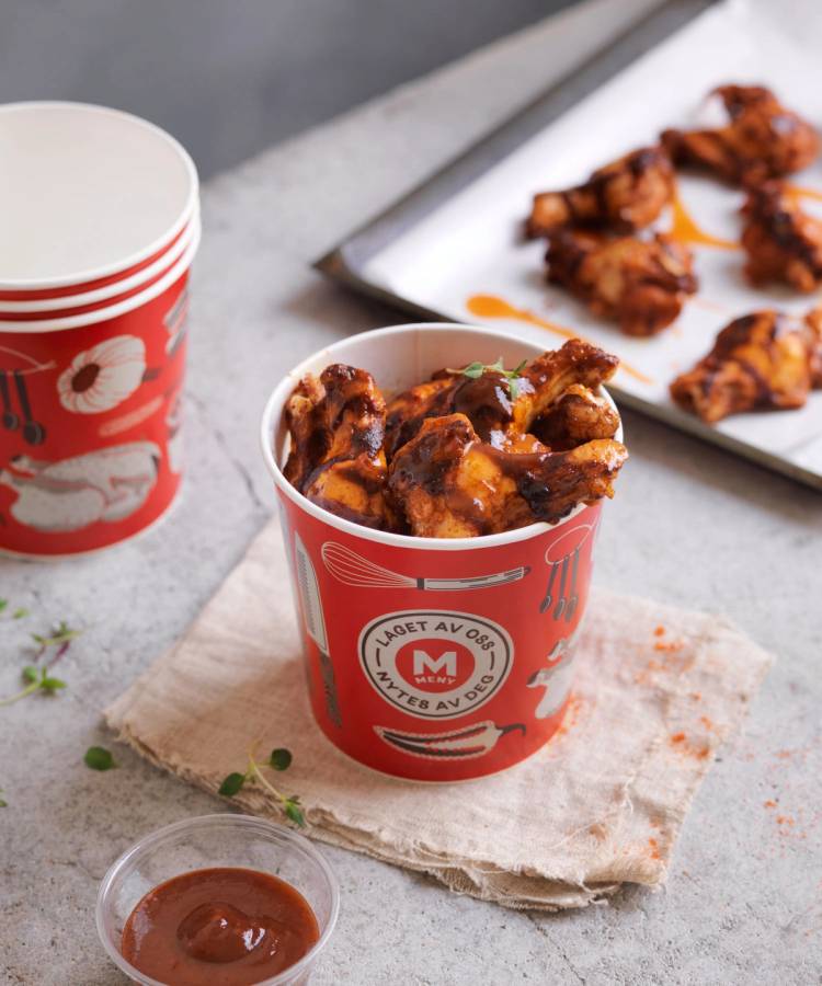 Kopper med buffalo wings og en tallerken med flere kyllingvinger på et bord, med en liten skål med saus ved siden av.