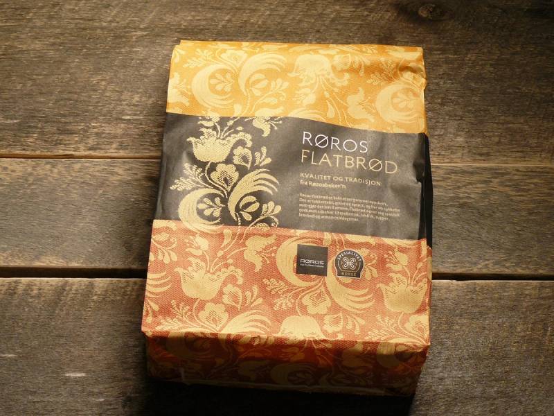 Pakke med Røros flatbrød i papirinnpakning med tradisjonelt mønster, plassert på en trebordflate.
