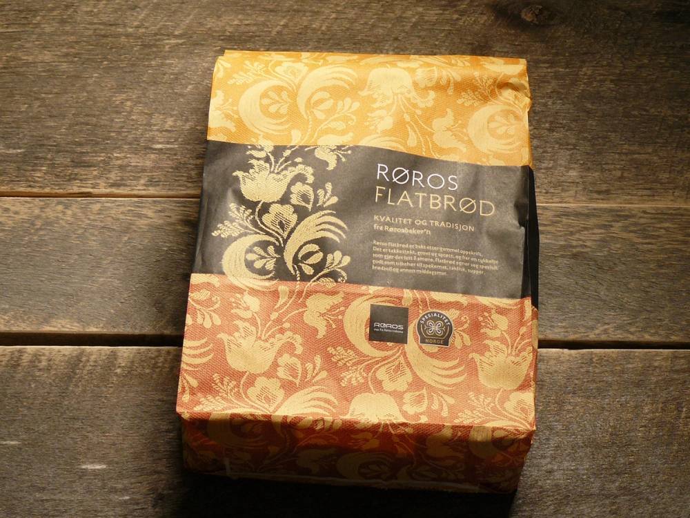 Pakke med Røros flatbrød i papirinnpakning med tradisjonelt mønster, plassert på en trebordflate.