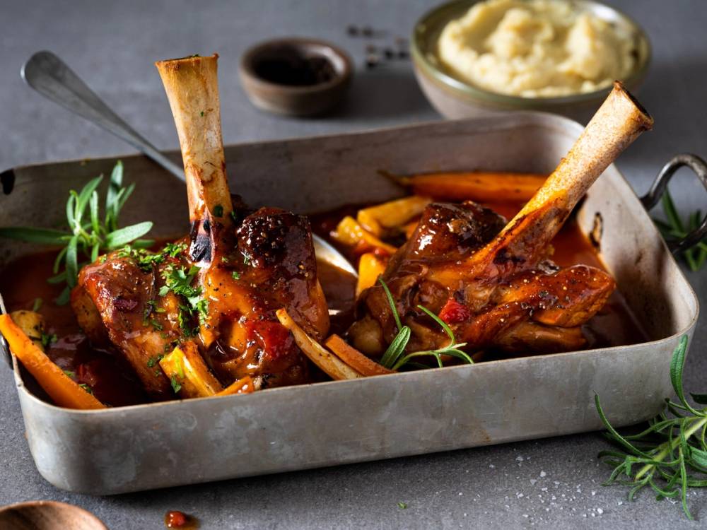 Lammebiter med rotgrønnsaker og en skål med potetmos på et fat, klar til servering.