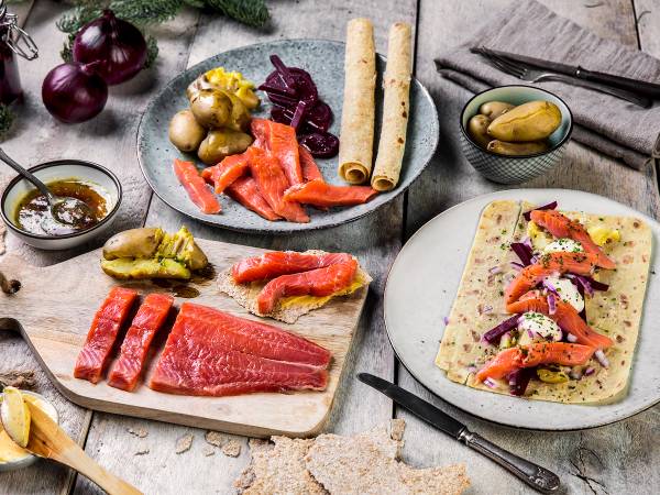 Rakfisk, flatbrød, og tilbehør på et bord, med noen rødløk og en liten skål med sylteagurk, som er typisk for et rakfisklag.