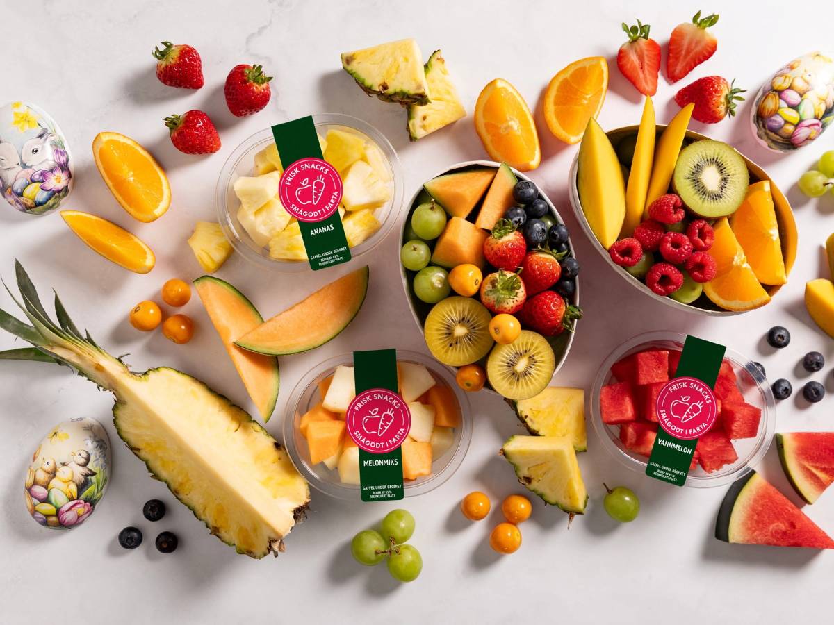 Fargerik fruktfat med vannmelon, druer, jordbær, kiwi, ananas, og små kaker med fruktdekor, samt noen pakker med fruktjuice.