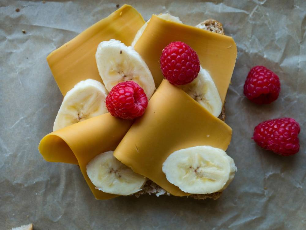 Skiver av brunost med bananskiver og friske bringebær på et papirark