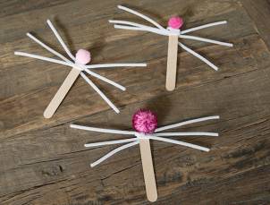 Tre påskeharer laget av trepinner, papir og små pom-pomer ligger på en treoverflate.