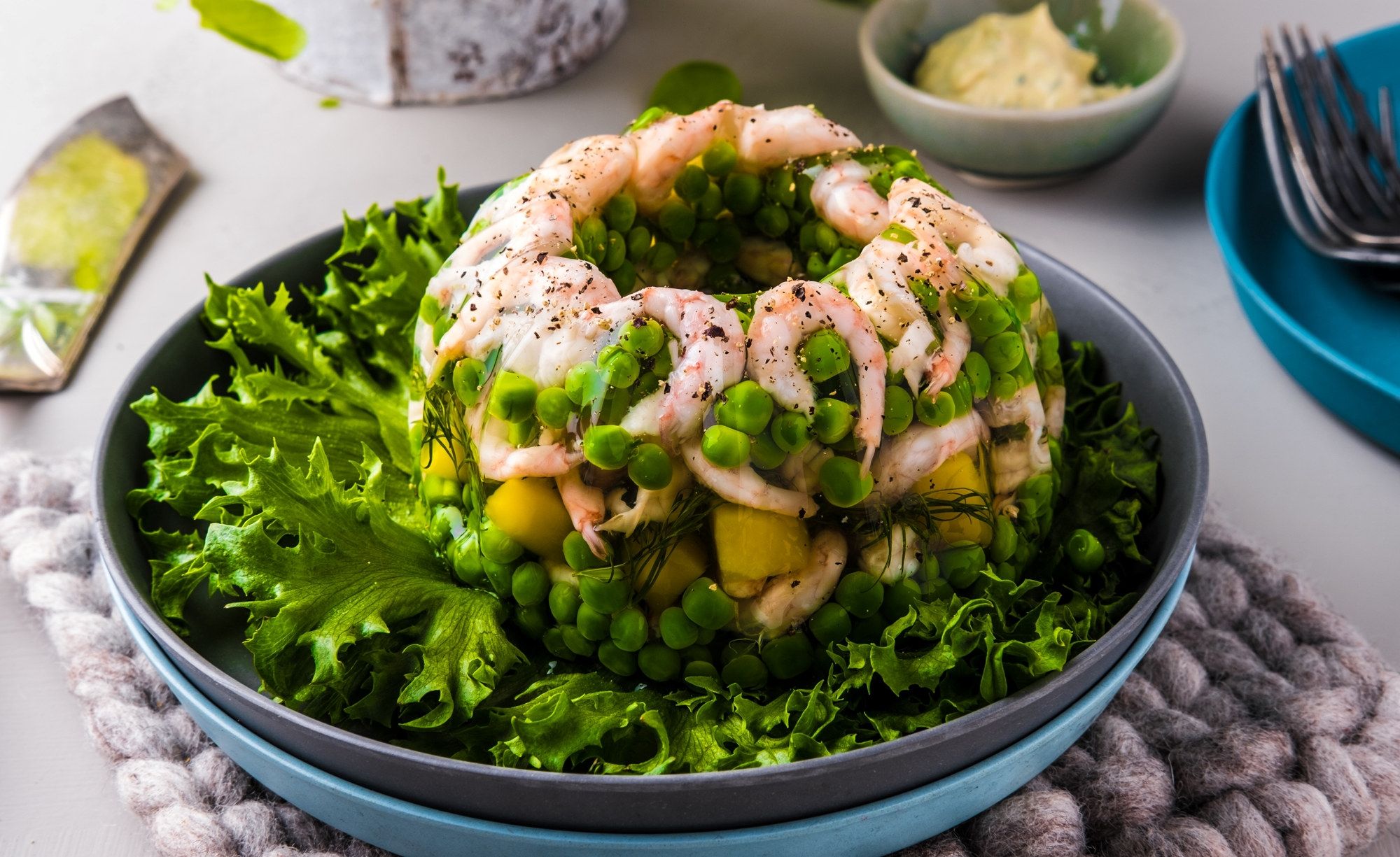 En salat med reker, avokado og grønnsaker servert i en bolle, med salatblad rundt og tilbehør på bordet.