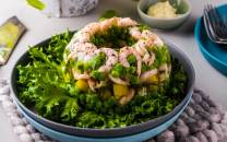 En salat med reker, avokado og grønnsaker servert i en bolle, med salatblad rundt og tilbehør på bordet.