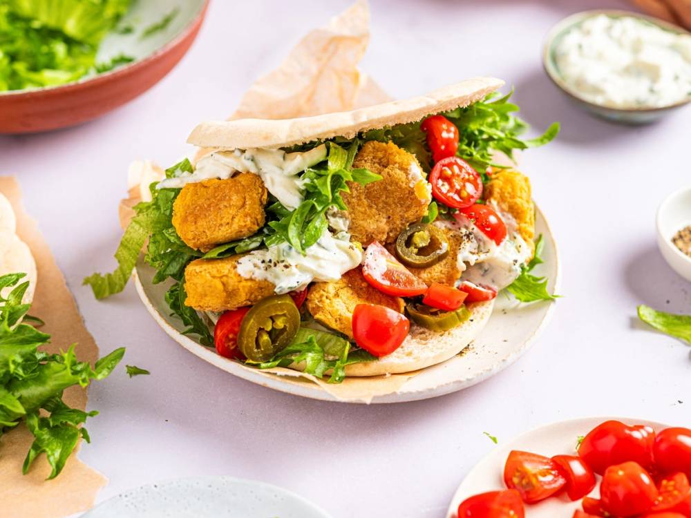 Falafel i pita med salat, tomater og dressing, omgitt av små skåler med saus og grønnsaker