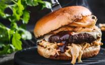 En saftig burger med kjøtt, ost, løk og dressing i et briochebrød på en grillrist.