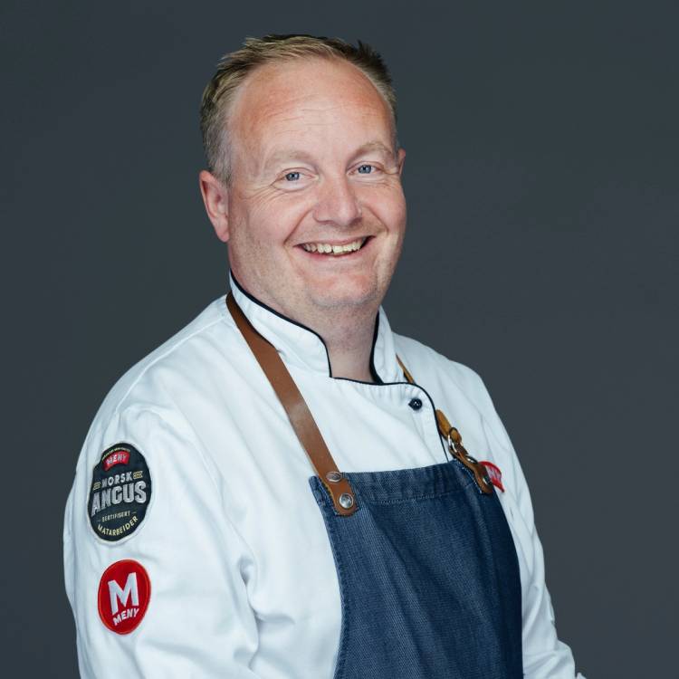 En person iført hvit kokkejakke og blå forkle, med en bakgrunn i mørk grå farge.