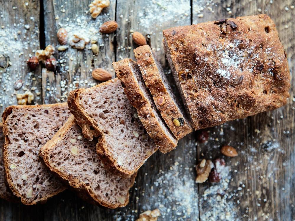 Grovbrød med nøtter som er skåret i skiver og lagt på en treplate med noen nøtter rundt, på et rustikt treoverflate.