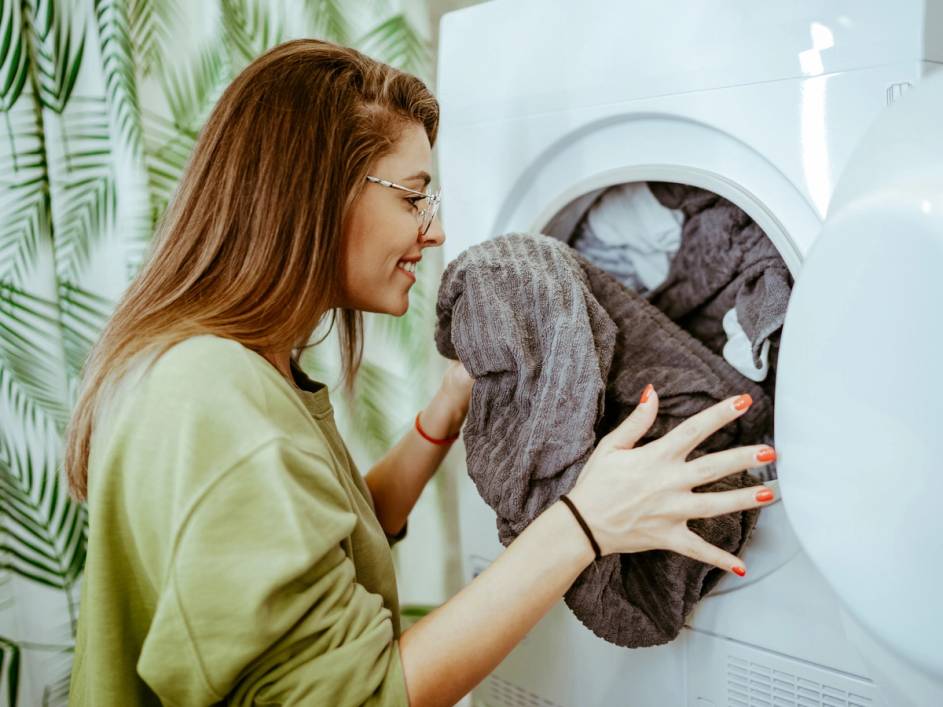 En person legger klær inn i en vaskemaskin, med fokus på klærne og maskinen.