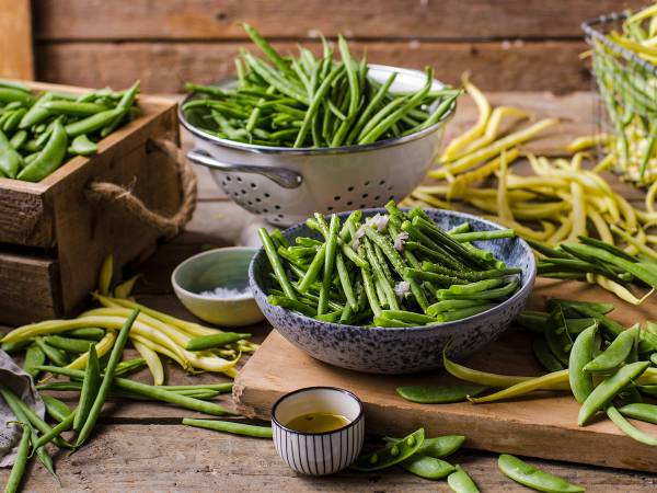 Ferske grønne bønner i ulike skåler og på bordet, med en liten skål med olje eller saus ved siden av.
