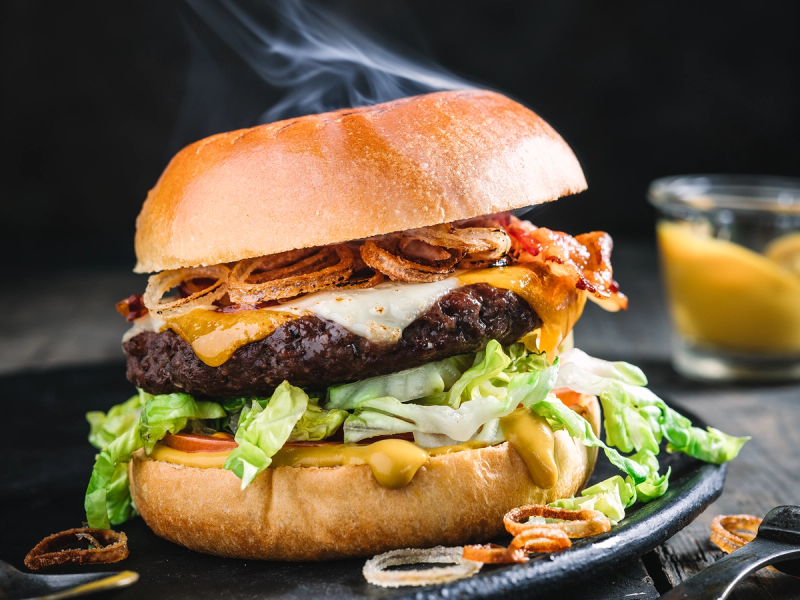 En saftig hamburger med bacon, ost, salat og dressing i et hamburgerbrød, klar til å spises.