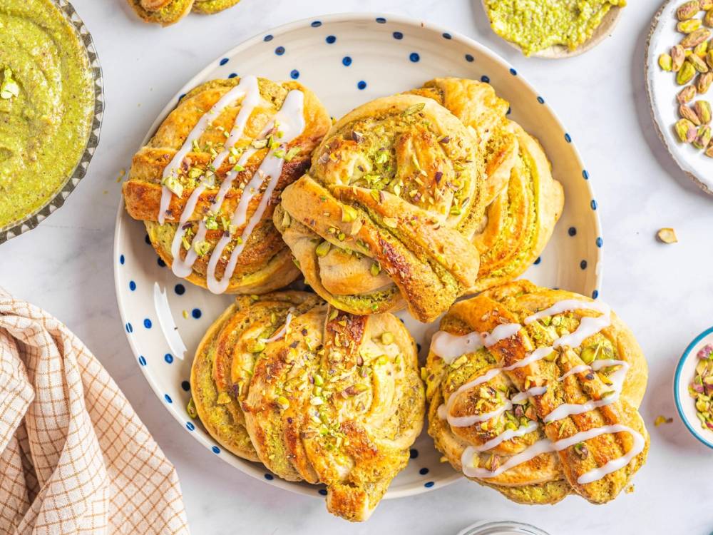 Pistasjboller med hvit glasur og hakkede pistasjnøtter på en hvit tallerken med blå prikker