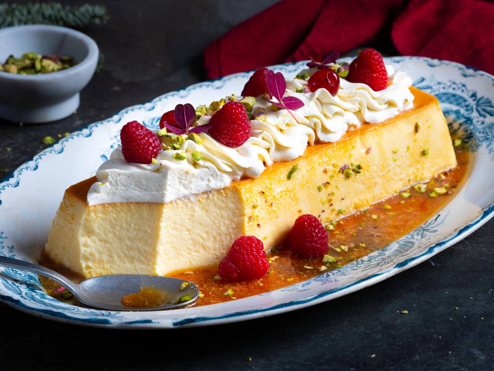 Karamellpudding med krem, jordbær og spiselige blomster på et serveringsfat.