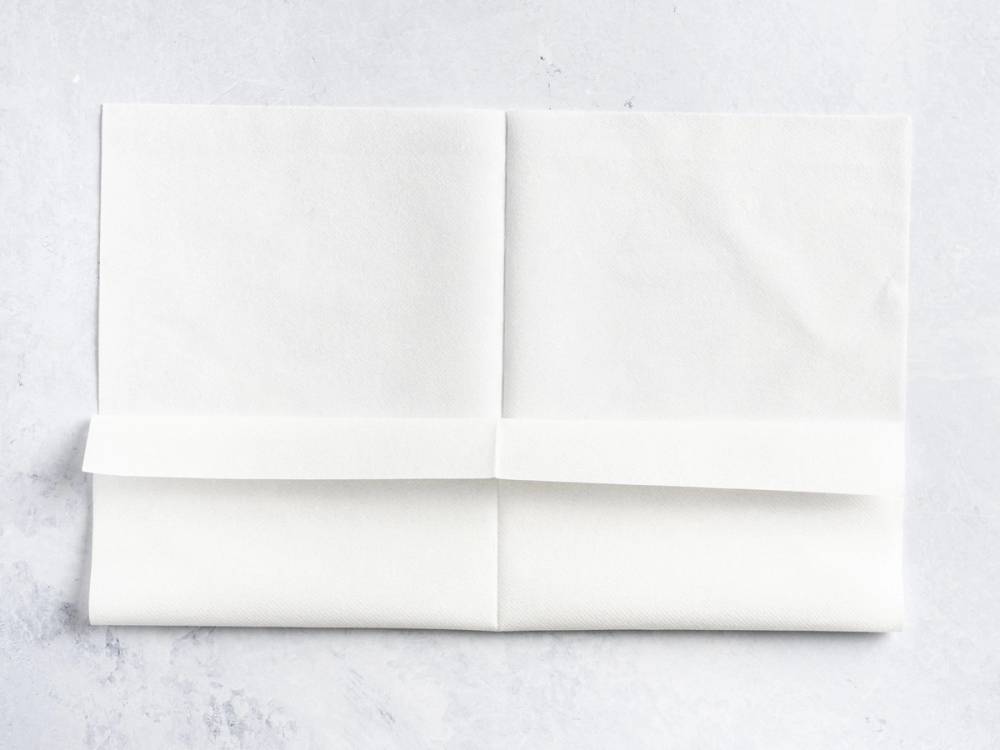En hvit serviett brettet i en lommeform, lagt på en hvit overflate.