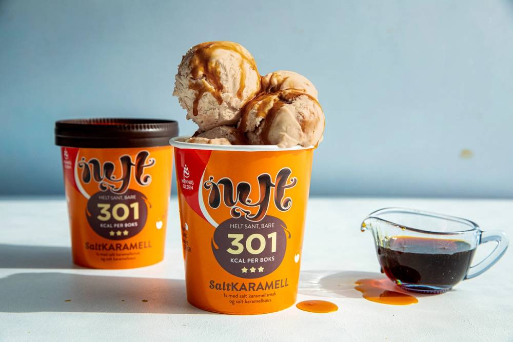 To små bøtter med salt-karamell iskrem og en liten kopp med karamellsaus på et bord mot en blå bakgrunn.