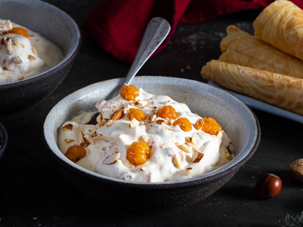 Multekrem i en skål med kokosflak og en skje, omgitt av vafler på et mørkt bord