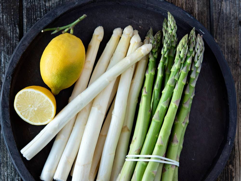 Ferske hvite asparges og en sitron på en svart tallerken