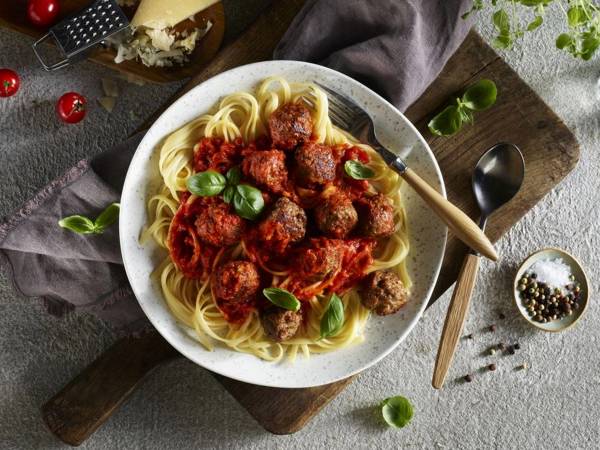 Kjøttboller i tomatsaus servert med spaghetti og basilikum på en tallerken.