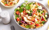 Fargerik pastasalat med fusilli, kyllingbiter, cherrytomater, agurk og salat i en stor bolle.