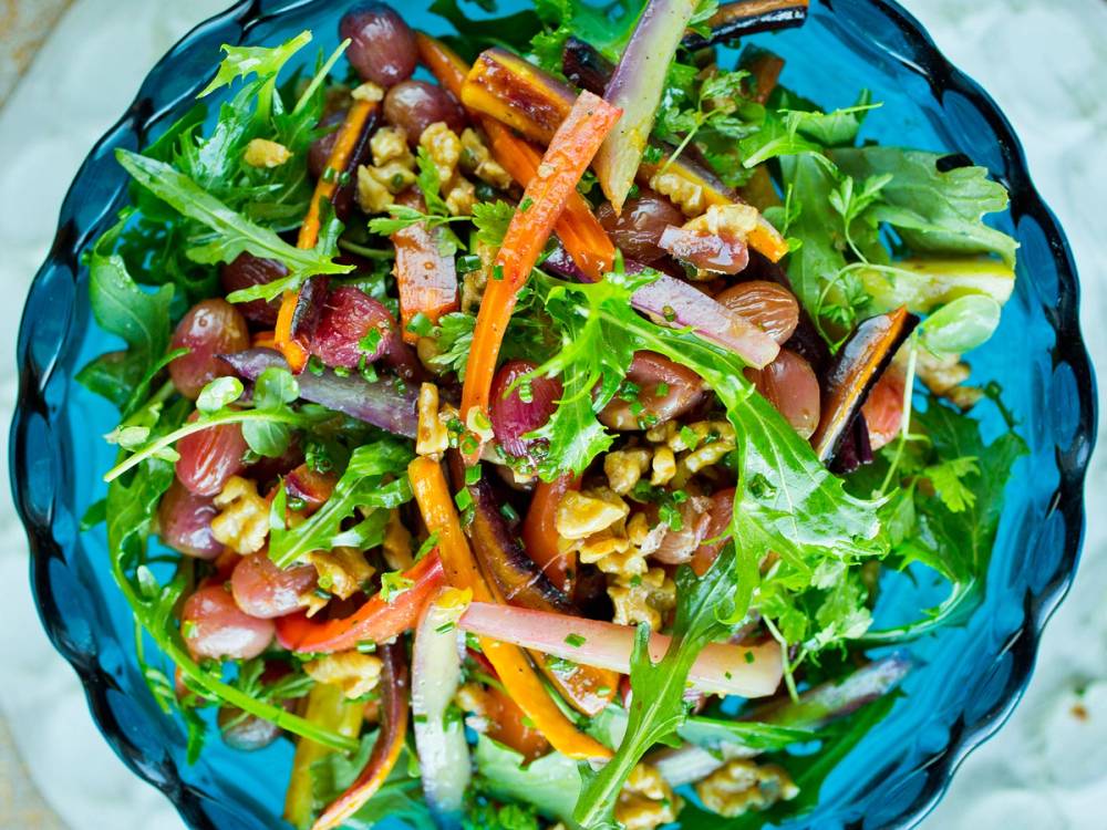 En varm salat med bakt gulrøtter, grønne blader og nøtter på en blå tallerken.