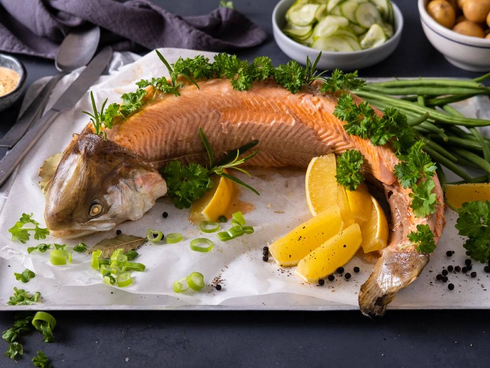 Helkokt ørret med sitronbåter og grønne urter på en hvit serveringsplate.