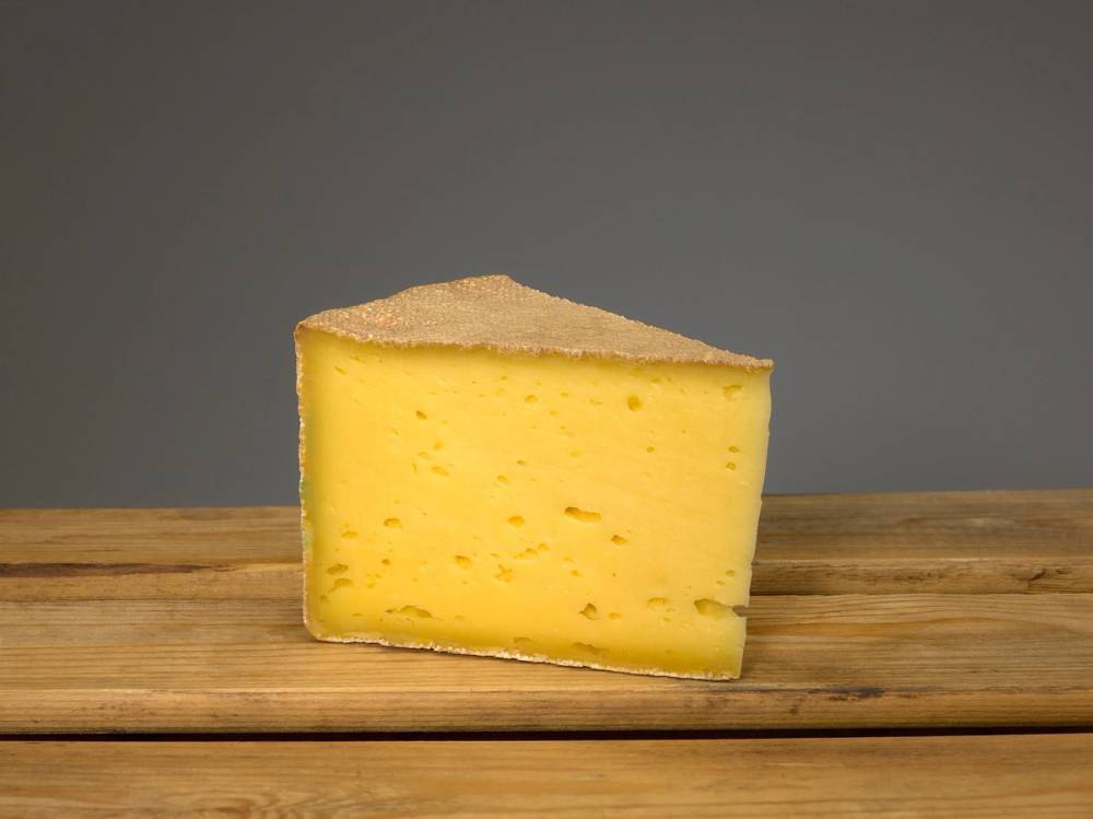 Et stykke gul ost på en treplate med en grå bakgrunn.