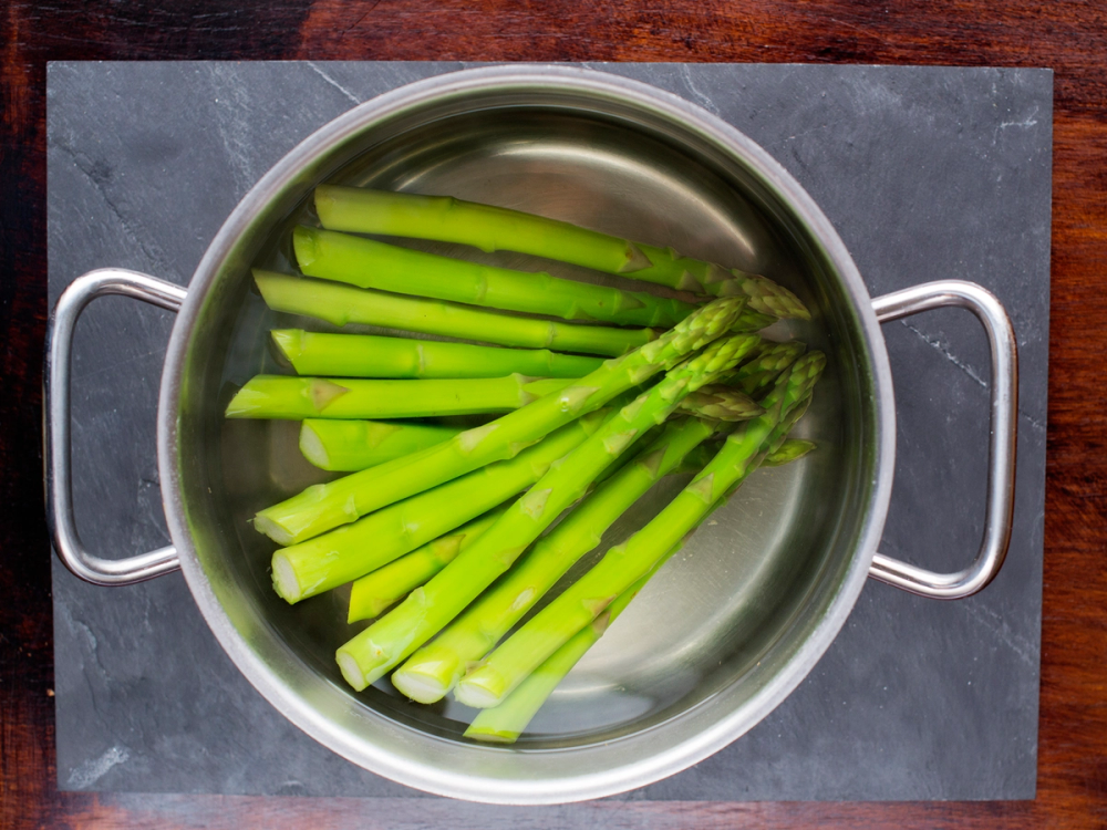 Grønne asparges kokes i en stålgryte på en svart steinplate.