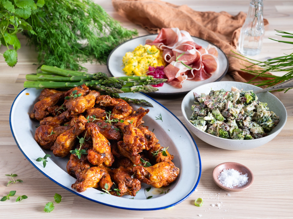 Koldtbord med kyllingvinger, salat, spekemat, potetsalat og grønnsaker på et bord.