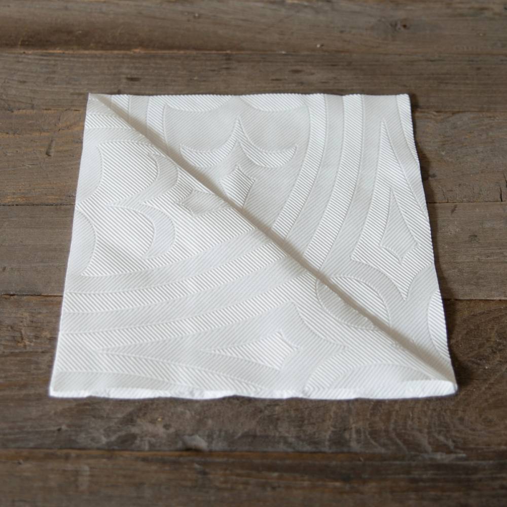 En hvit juleserviett med dekorative mønstre ligger brettet på en treflate.