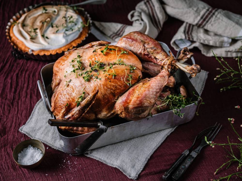 Stekt kalkun med krydderurter på et serveringsfat, omgitt av tilbehør og pynt til Thanksgiving-middag